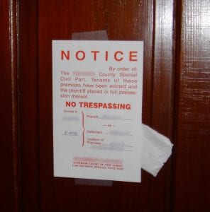 A notice in red letters is taped to a wooden door. It reads "Notice: by order of the [blanked out] County Special Civil Part. Tenants of these premises have been evicted and the plaintiff placed in full possession thereof. NO TRESPASSING."