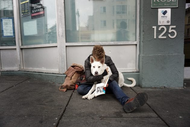 A person hugs a white dog on the streets.
