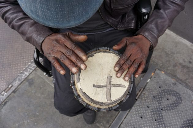 A photograph by Visions of Justice student Christopher Shurn. The image shows two hands hitting a drum with a black X on it.