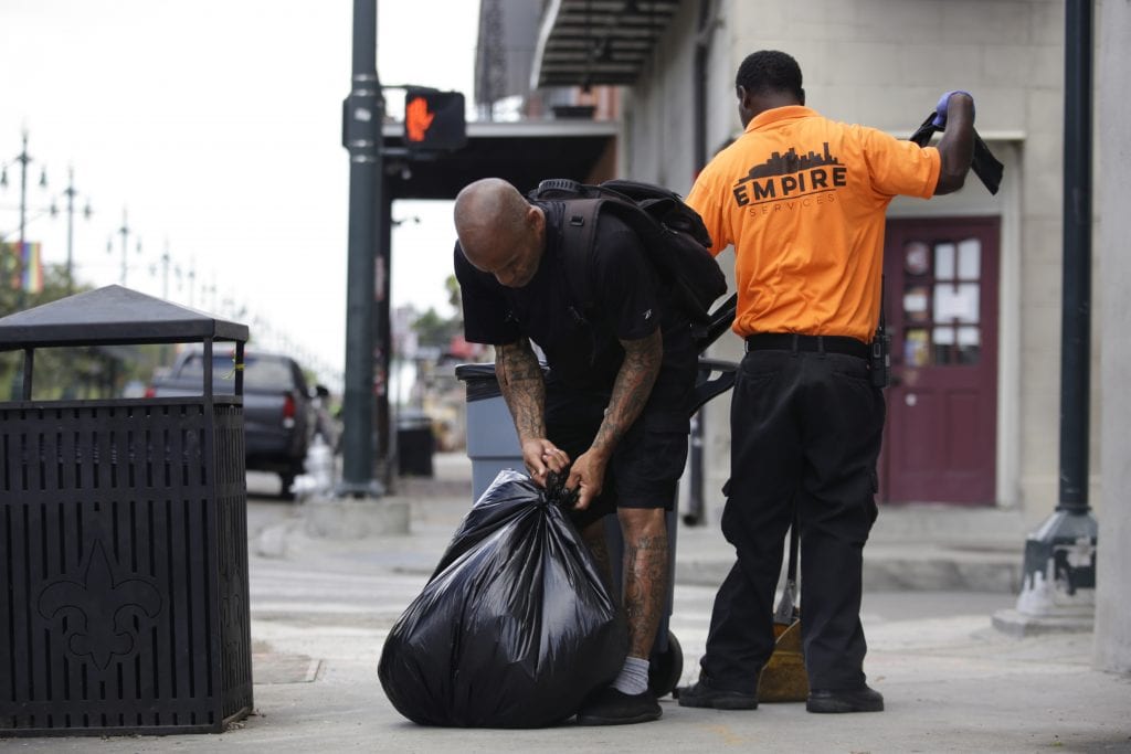 A man in black ties up a black garbage bag. He is a sanitation worker who was kicked out of his home during the pandemic for paying rent late.