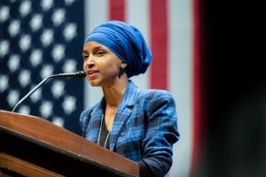 Rep. Ilhan Omar, who stands at a podium in front of an American flag, has proposed legislation that would cancel rent and individual mortgage payments nationwide to deal with the COVID-19 crisis.