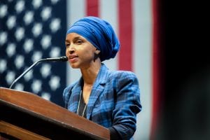 Rep. Ilhan Omar, who stands at a podium in front of an American flag, has proposed legislation that would cancel rents and individual mortgage payments nationwide to deal with the COVID-19 crisis.