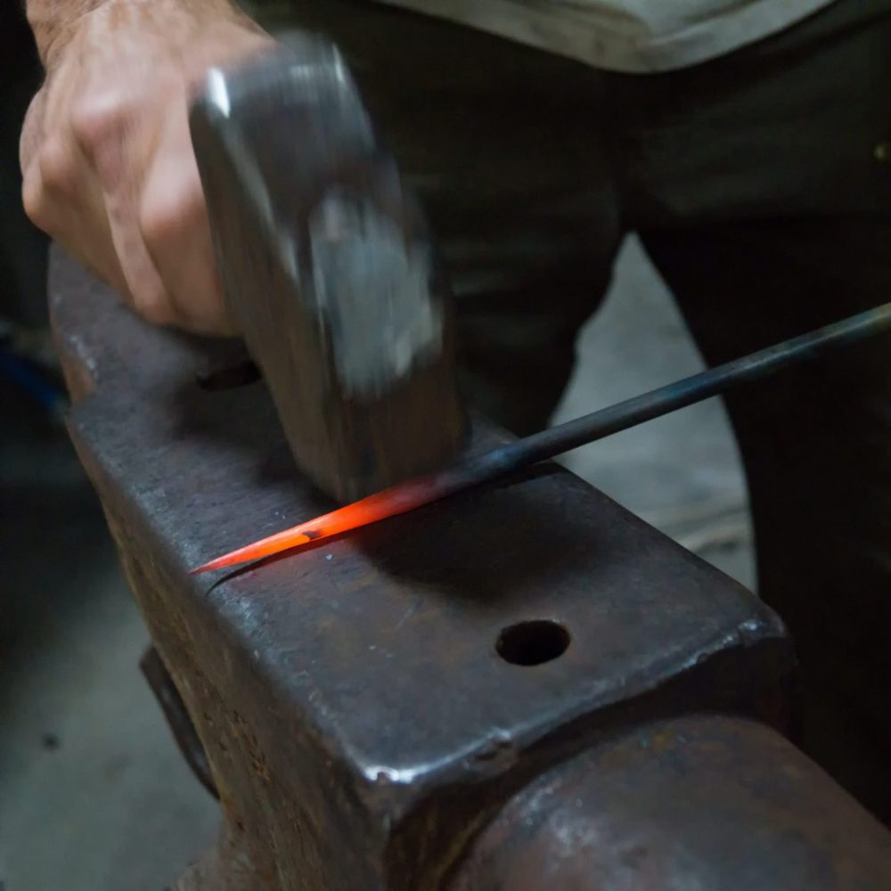 Blacksmith hammering iron on anvil