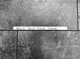 Tape sign on stone floor: Wait your turn here