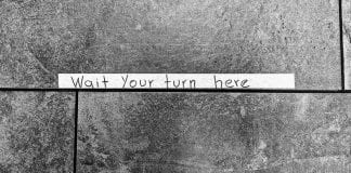 Tape sign on stone floor: Wait your turn here