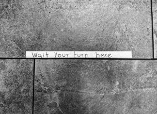 Tape sign on stone floor: Wait your turn here