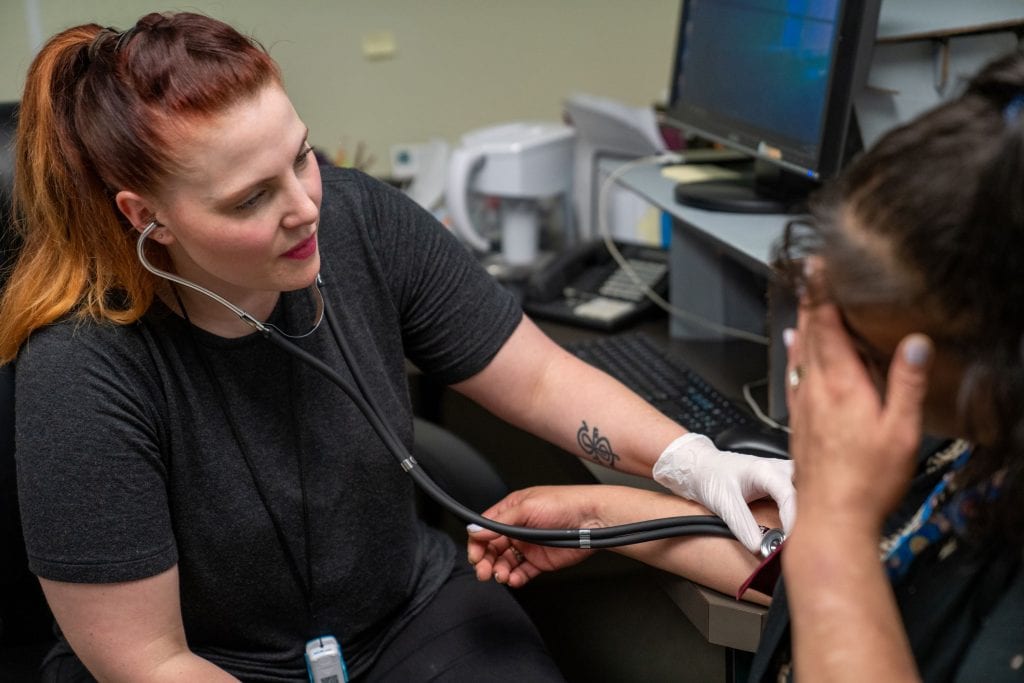 hotel rooms for the homeless are healthier than congregate housing. A nurse takes a homeless woman's blood pressure