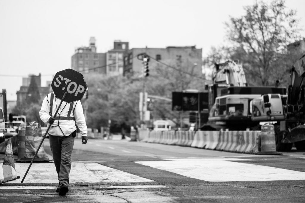 in New York, a person walks to the left holding a stop sign.