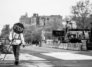 in New York, a person walks to the left holding a stop sign.