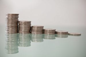 Stock photo of six stacks of quarters on a glossy surface, with a tall stack at the left and each succeeding stack a bit shorter, till the fifth one is just one coin.