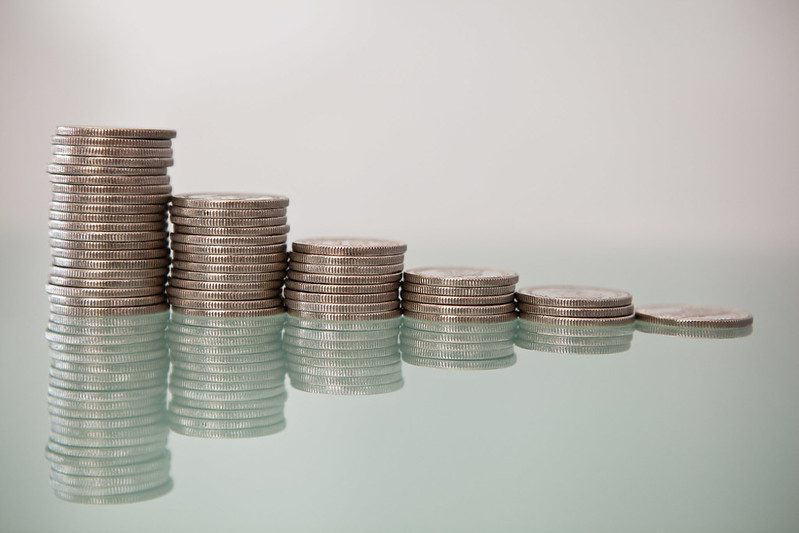 Stock photo of six stacks of quarters on a glossy surface, with a tall stack at the left and each succeeding stack a bit shorter, till the fifth one is just one coin.