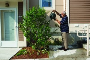 nonprofit housing: image shows man watering plant in front of nonprofit apartment building