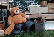 A teddy bear sits among discarded furniture on the side of the street