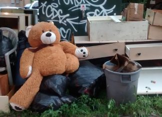 A teddy bear sits among discarded furniture on the side of the street