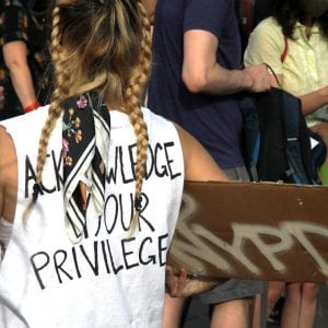 Person at a protest wears a shirt that says, "Acknowledge your privilege"