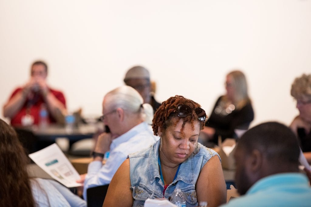 A group of community members sit at tables reading papers.