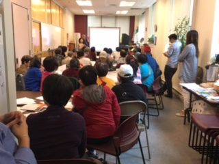 photos shows view from back of room at well-attended community meeting on in Chinatown, Boston. 