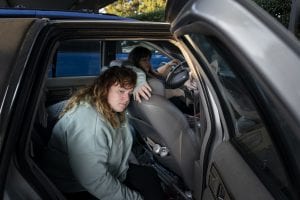 A girl leans against the seat of a car, seemingly tired. Family homelessness