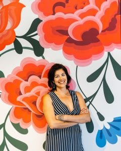 Photo of Irma Robinson, co-owner of a catering business helped by Pacific Community Ventures, standing before a large floral backdrop. PCV focuses its work on good job creation.