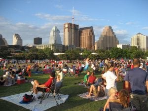 A crowd of people relaxing in an Austin, Texas, park in the evening, with the city skyline visible in the background, accompanying an article on cities with a high rate of population growth.