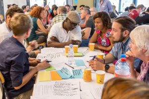 Six people sit at a table, with papers, pencils, and cups on the table top. They're at the founding meeting of the resident association of their nonprofit cooperative in Zurich.