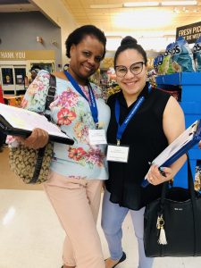 Two women stand together in a supermarket, both holding clipboards and wearing nametag lanyards, both participating in the Healthy Neighborhoods Study in Lynn, Mass.dy