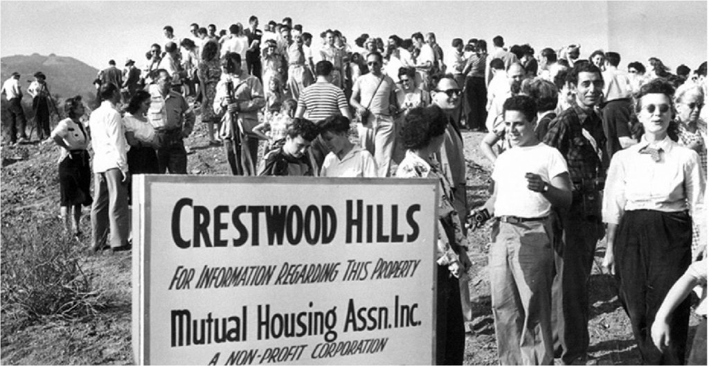 A black-and-white photo showing a large group of milling people near a sign that reads "Crestwood Hills/For information regarding this property/Mutual Housing Assn. Inc."