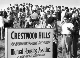 A black-and-white photo showing a large group of milling people near a sign that reads "Crestwood Hills/For information regarding this property/Mutual Housing Assn. Inc."