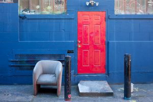 A bright red door contrasts strongly with the blue of the wall, in a cropped photo of a building. Illustrating an article about Democratic housing policies