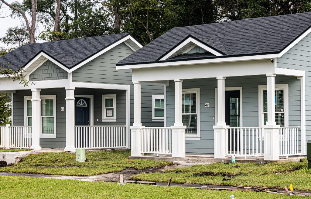 Two cottages, both painted gray with white trim and front porches with white railings. They are two of 50 in a tiny home project in Jacksonville, Florida.