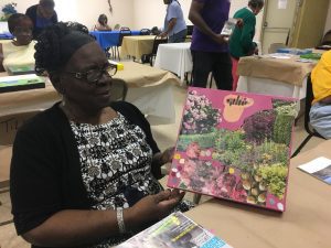 A woman holds a painting she created of lush flowers and greenery.