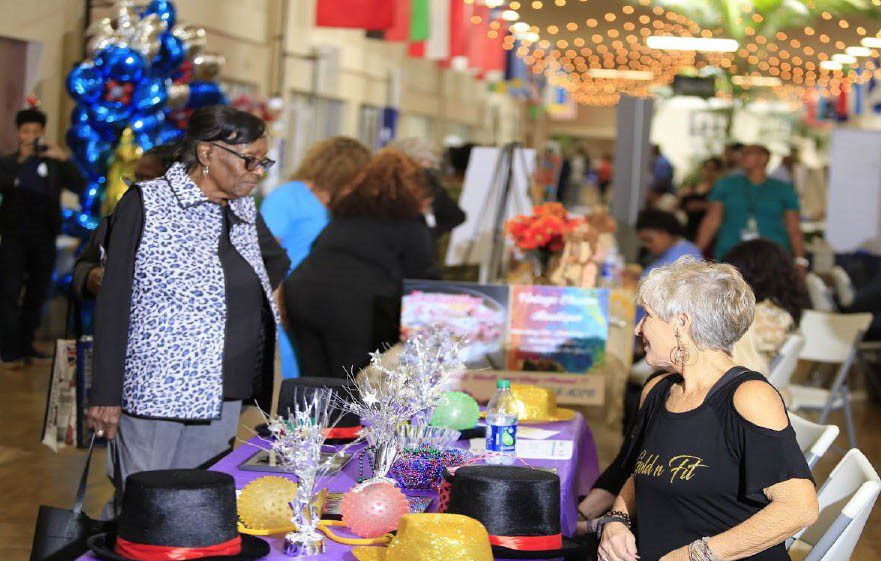 Two older woman talk at a table, as part of a busy outreach event.