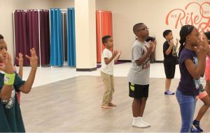 Children standing with their hands in front of their faces, learning a dance.