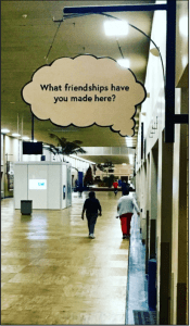 A plywood thought bubble reading "What friendships have you made here?" hangs on the wall of the Medical Mall as two community members are pictured behind it.