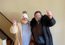 Two women in jackets and face masks hold up keys.