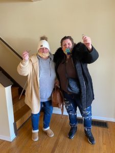 Two women in jackets and face masks hold up keys.