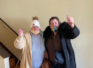 Two women in jackets and face masks hold up keys.