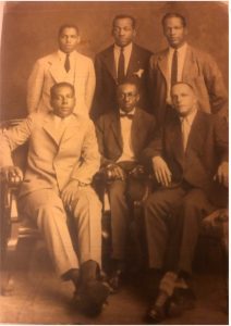 Six men, including James A. Parsons, at left, in a historical photo. Three men are standing behind three men who are sitting on chairs. James, the man at left, generated untold wealth for the Duriron Company yet he was blocked from generating wealth to pass down to his family.