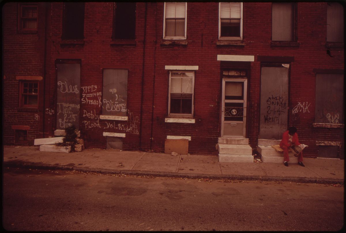 Two men sit on stoops of rowhomes in 1970s Philadelphia