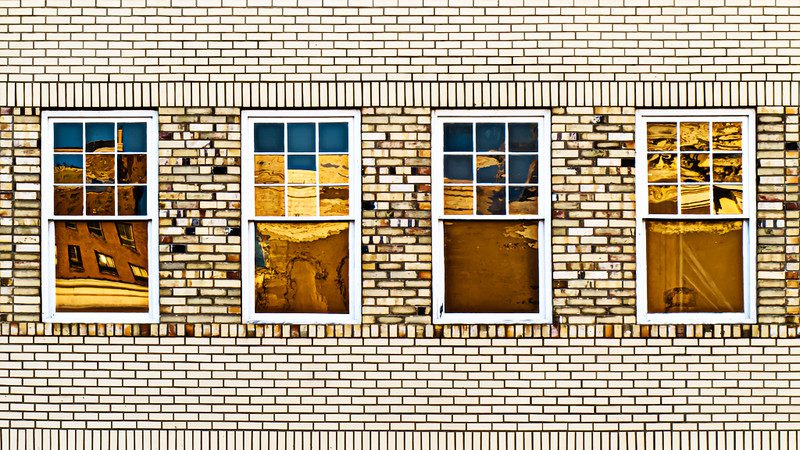 Exterior view of a pale-brick city building, four windows in a row. The light reflects off each window slightly differently, giving each one a different look. Illustrating an article about Faircloth-to-RAD program