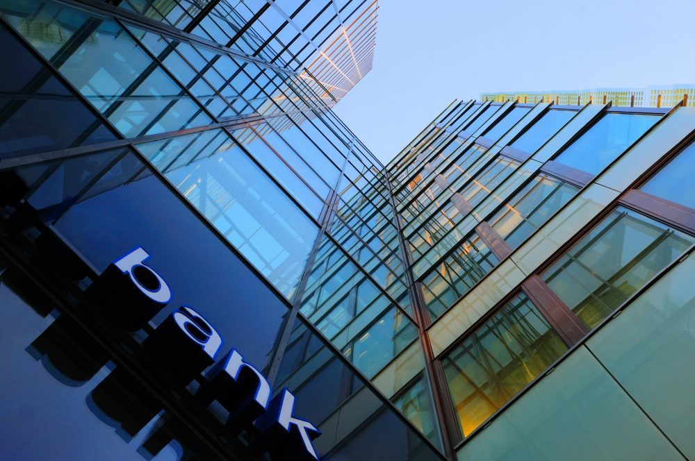 Bank corporate finance building seen from below. The sign "bank" visible close. Sky reflecting in the glass facade. More Facade pictures below