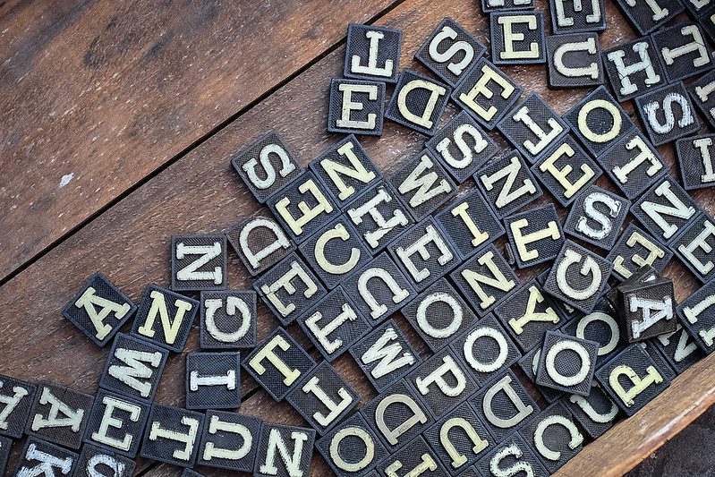 A jumble of black tiles with white uppercase letters on a brown wooden table, for an article on acronyms in the community development field