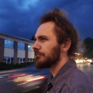 Profile photo of Doug Farrand, co-organizer of Music City. Farrand is outdoors, near a street, looking off to the left. He's wearing a gray shirt and has a full beard. 