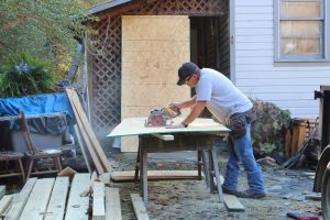 A construction worker cuts a piece of wood in front of a house.