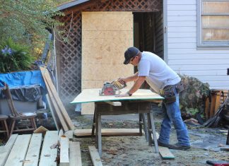 A construction worker cuts a piece of wood in front of a house.