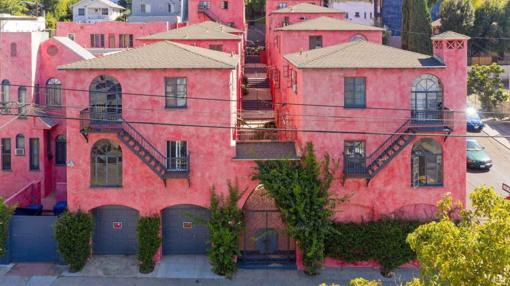 An exterior view of three-story apartment buildings in a bright raspberry-pink color. An example of a new way of building community wealth.