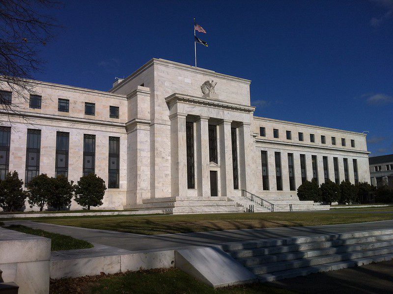 An exterior view of the Federal Reserve building. The white granite of the building contrasts with the deep-blue sky behind it.