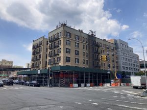 A view from across the street of a corner building in the Bronx that's being renovated. A green construction awning is set up on both sides of the building. 