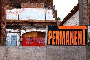 Photo of a disused theater, showing dilapidated exterior. Someone has hung an orange-on-black sign reading "Permanent" on the wooden barrier. Illustrating article on the harm unsealed eviction records can do.
