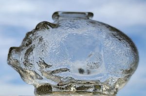 A glass piggybank photographed against the sky with the blue showing through it, illustrating salary transparency.